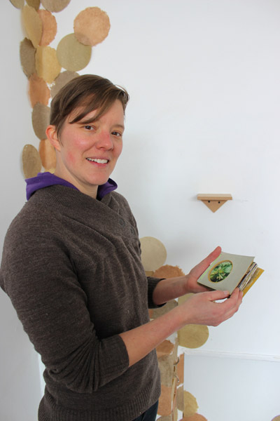 Heeres, displaying one of her handmade books, in front of a wall of paper circles, in a recent group show at Public Pool.